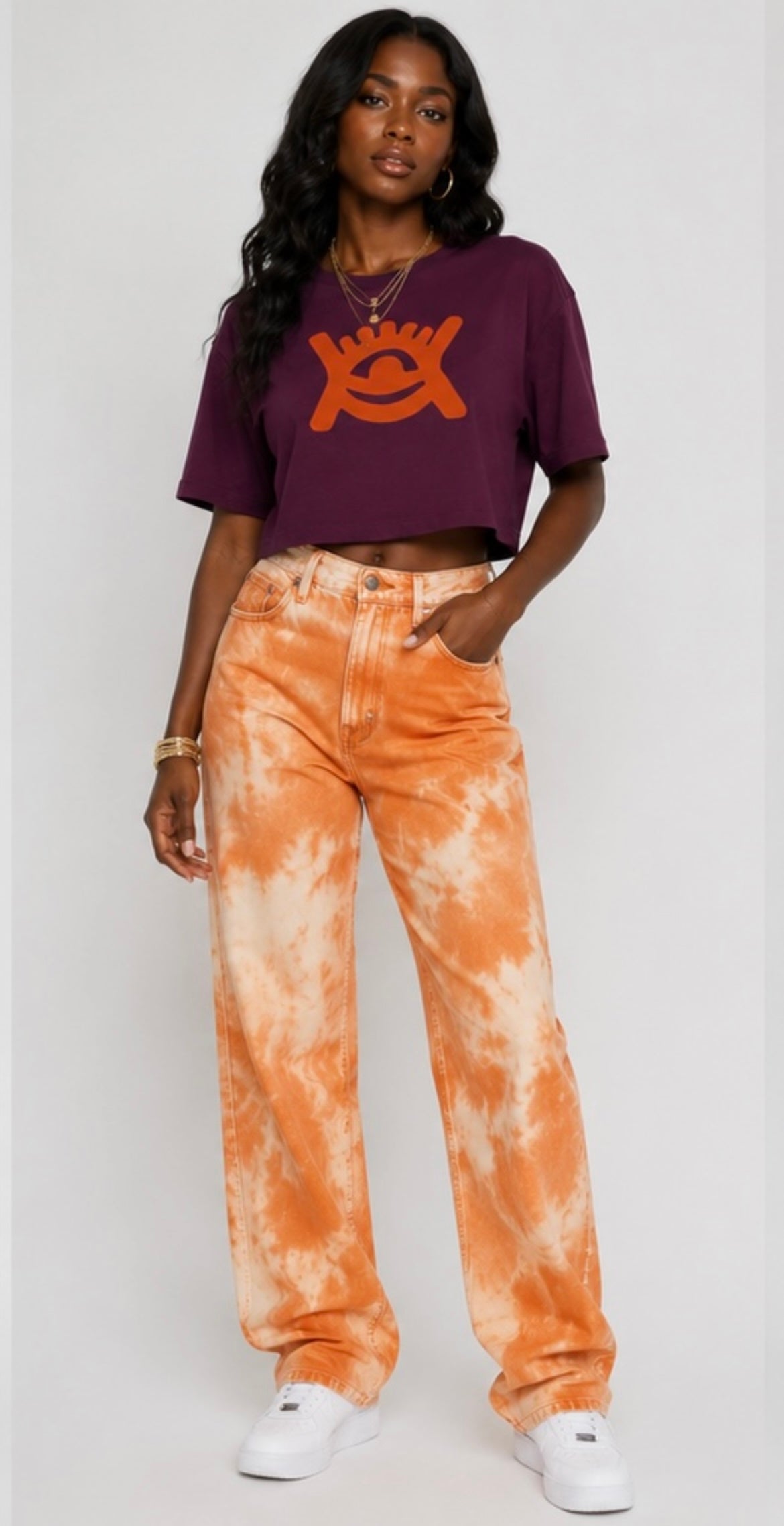 Model wearing cropped mulberry coloured top, wearing orange jeans and white trainers. 