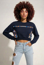 Person wearing a black sweatshirt with colorful patterns and light blue jeans on a plain background