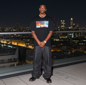 Person wearing a black t-shirt with 'DESIRES' text, standing on a rooftop at night with city lights in the background.