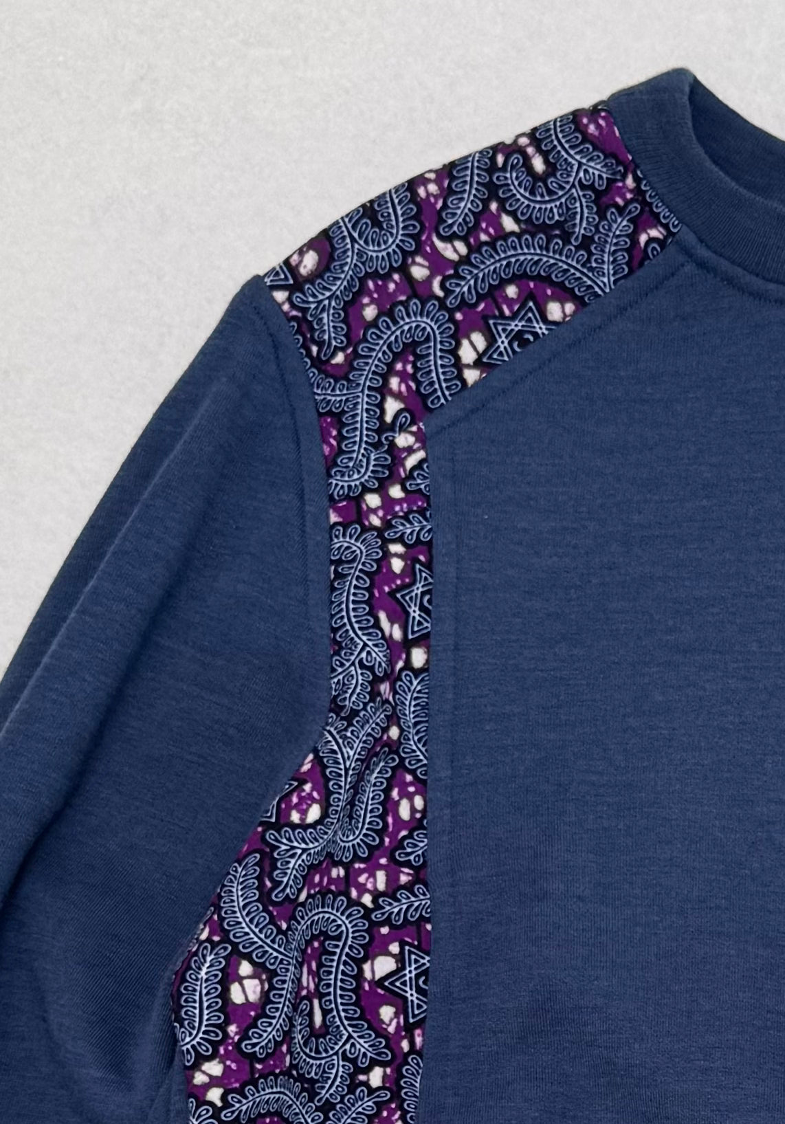 Blue sweater with purple and black patterned sleeves on a light gray background