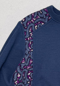 Blue sweater with purple and black patterned sleeves on a light gray background
