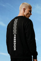 Person wearing a black sweatshirt with 'FREEDOM' printed on the back against a blue sky.