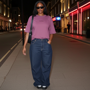 Person wearing a purple t-shirt and blue jeans standing on a city street at night.