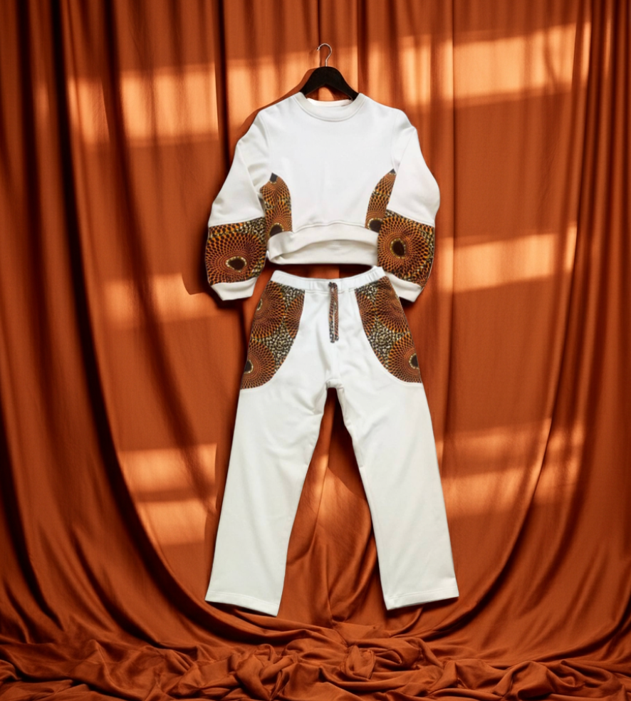 White outfit with brown patterned sleeves and pants on a hanger against a brown curtain.