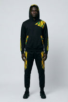 Person wearing a black hoodie and pants with yellow and green patterns on a white background